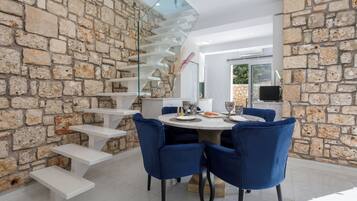 A dining area with a stone wall, a glass staircase, and blue chairs.
