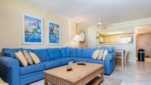 A living room with a blue sofa, a wooden coffee table, and two paintings on the wall. - Shoreham Towers I - C3 (North Myrtle Beach)