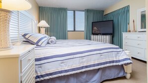 A hotel room with a bed, a TV, a dresser, and a window with curtains. - Shoreham Towers I - C3 (North Myrtle Beach)