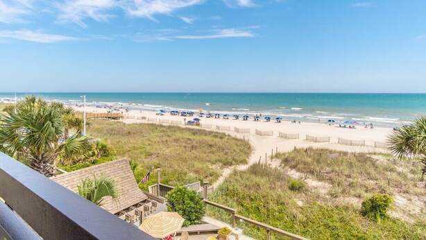 A beach view from a balcony overlooking a sandy beach with a clear blue sky. - Shoreham Towers I - C3 (North Myrtle Beach)