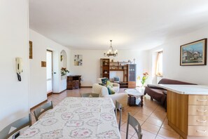 A spacious living area with a dining table, a sofa, a kitchen area, and a chandelier.