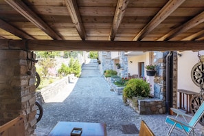 A stone-paved courtyard with a wooden pergola, rustic stone walls, and hanging flower baskets.