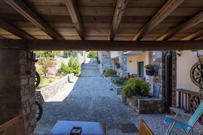 Un patio empedrado con un pérgola de madera, muros de piedra y macetas colgantes.