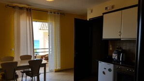 A compact kitchen with a refrigerator, stove, and microwave. There is a dining area with chairs and a table, and a balcony with a view.