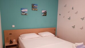 A neatly made bed with white linens and towels, a wooden headboard, a nightstand with a lamp, and three wall art pieces depicting landscapes.