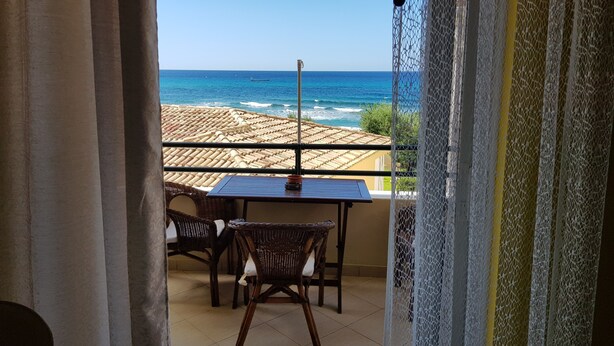 A balcony with a table and chairs, overlooking a coastal area with a view of the sea and buildings in the distance.