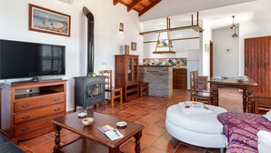 A living room with a television, wooden furniture, a fireplace, and a kitchen area with a tiled backsplash. - Air-conditioned Holiday Home with Patio, Pool, Wi-Fi and Lawn (Barbate)
