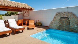 A pool area with lounge chairs, a wooden table, and a stone wall. - Air-conditioned Holiday Home with Patio, Pool, Wi-Fi and Lawn (Barbate)