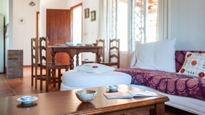 A room with a wooden table, a bed with patterned bedding, a dining area with chairs, and a window with a view. - Air-conditioned Holiday Home with Patio, Pool, Wi-Fi and Lawn (Barbate)