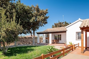 A white building with a tiled roof, a wooden fence, and a patio area with a grill.