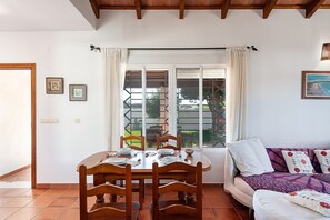 A dining area with a wooden table and chairs, a sofa with patterned cushions, and a window with curtains.