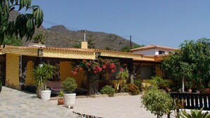 Un edificio de dos pisos con techo de tejas, rodeado de plantas en macetas y un patio empedrado.