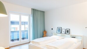 A bedroom with a bed, a desk, a chair, a window with curtains, and a wall-mounted light.