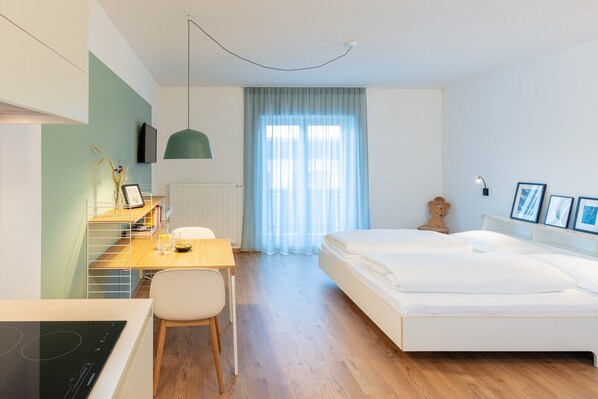 A modern hotel room with a wooden desk, a bed, a radiator, and a window with curtains.