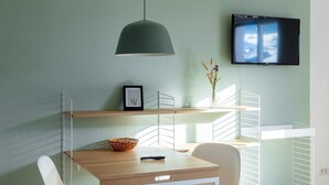 A modern dining area with a wooden table, white chairs, a hanging light fixture, and a mounted TV.