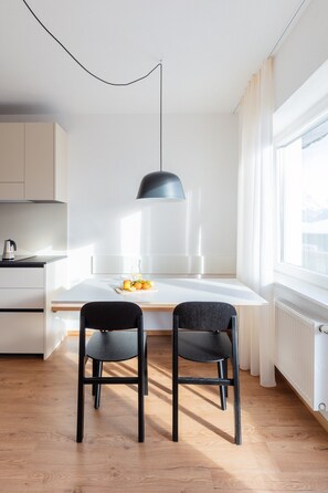 Cocina moderna con encimera blanca, dos sillas negras, lámpara colgante y ventana con cortinas.