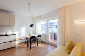 Una cocina moderna con una mesa de comedor y sillas, un sofá con un cojín y vistas a una montaña a través de amplias ventanas.