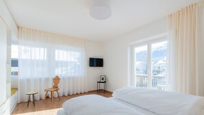 A hotel room with two beds, a TV, a small table, a chair, and a balcony with a view. - Modern "Hus Apartment - Nr. 2" with Balcony, Garden & Wi-Fi (Olang)
