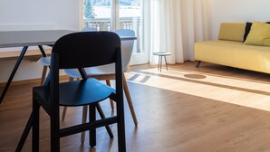 A modern living room with a sofa, a dining table with chairs, and a large window with curtains. - Modern "Hus Apartment - Nr. 5" with Balcony, Garden & Wi-Fi (Olang)