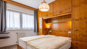 Een slaapkamer met een houten bed, een raam met gordijnen, een wandlamp en een radiator.