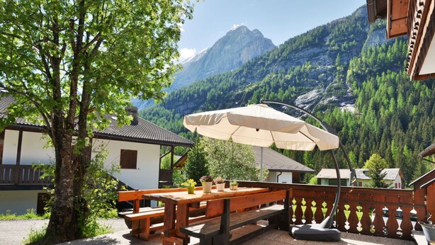 Een houten terras met picknicktafels en parasols, omgeven door een houten hek, met een berg op de achtergrond.