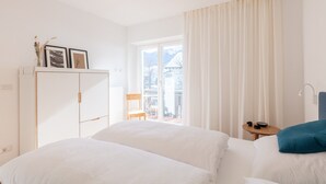 A hotel room with a bed, a small table, a chair, a wardrobe, and a window with curtains. - Modern "Hus Apartment - Nr. 3" with Balcony, Garden & Wi-Fi (Olang)