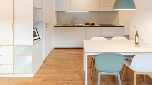 A modern kitchen with white cabinets, a wooden floor, and a dining area with a table and chairs. - Modern "Hus Apartment - Nr. 3" with Balcony, Garden & Wi-Fi (Olang)