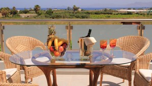 A glass-top table with wicker chairs, a fruit bowl, a bottle, and two glasses on a balcony overlooking a body of water and distant land. - Xenos Villa 1 With Private Swimming Pool Near The Sea (Kos)