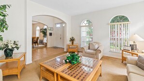Un salón amplio con una mesa de centro grande, un sofá y un mueble para televisión. Se observa un comedor al fondo con una mesa y sillas.