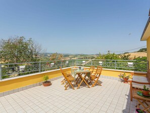Una terraza con mesa y sillas, plantas en macetas y vistas al campo.