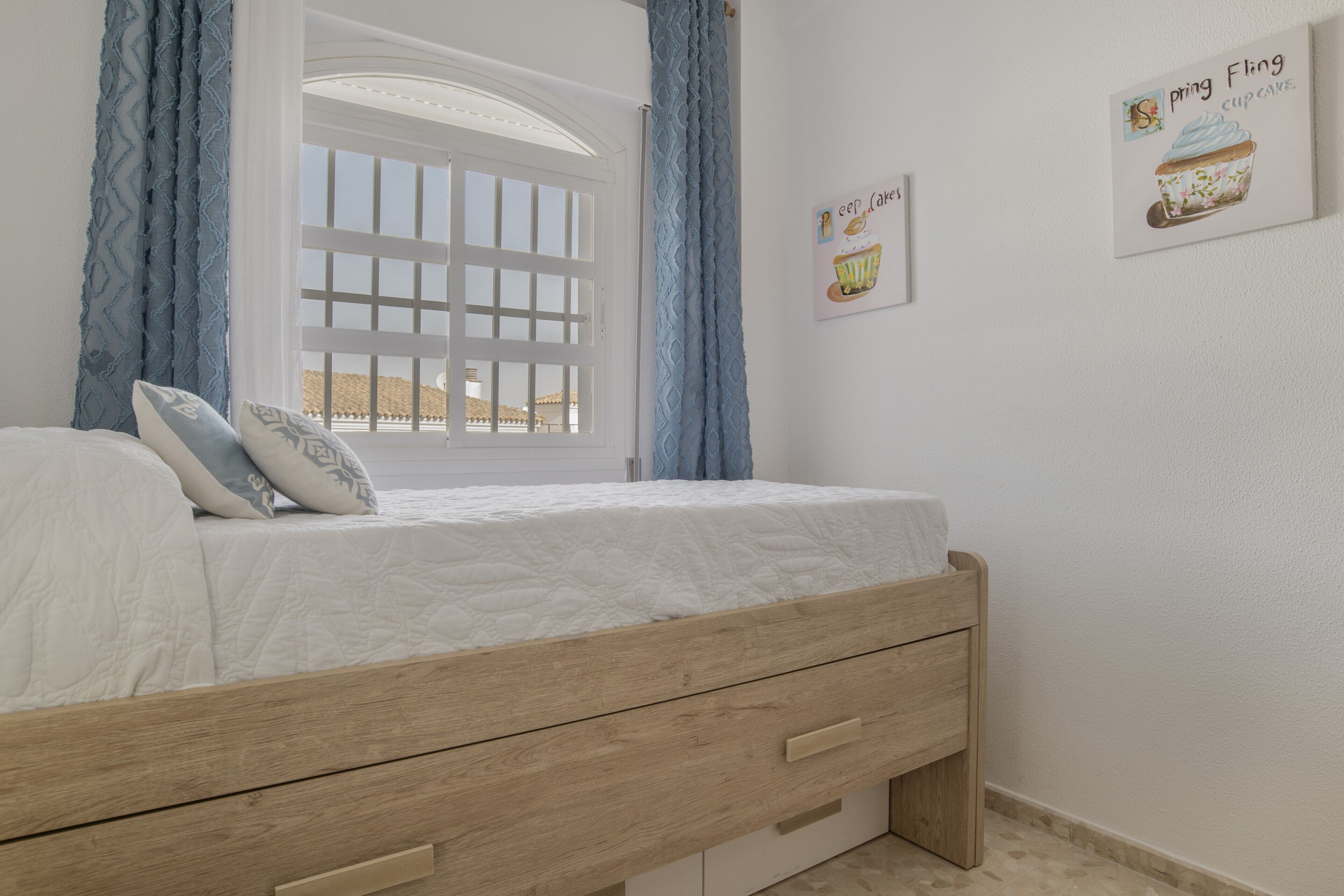 A bedroom with a wooden bed, a window with blue curtains, and wall art.