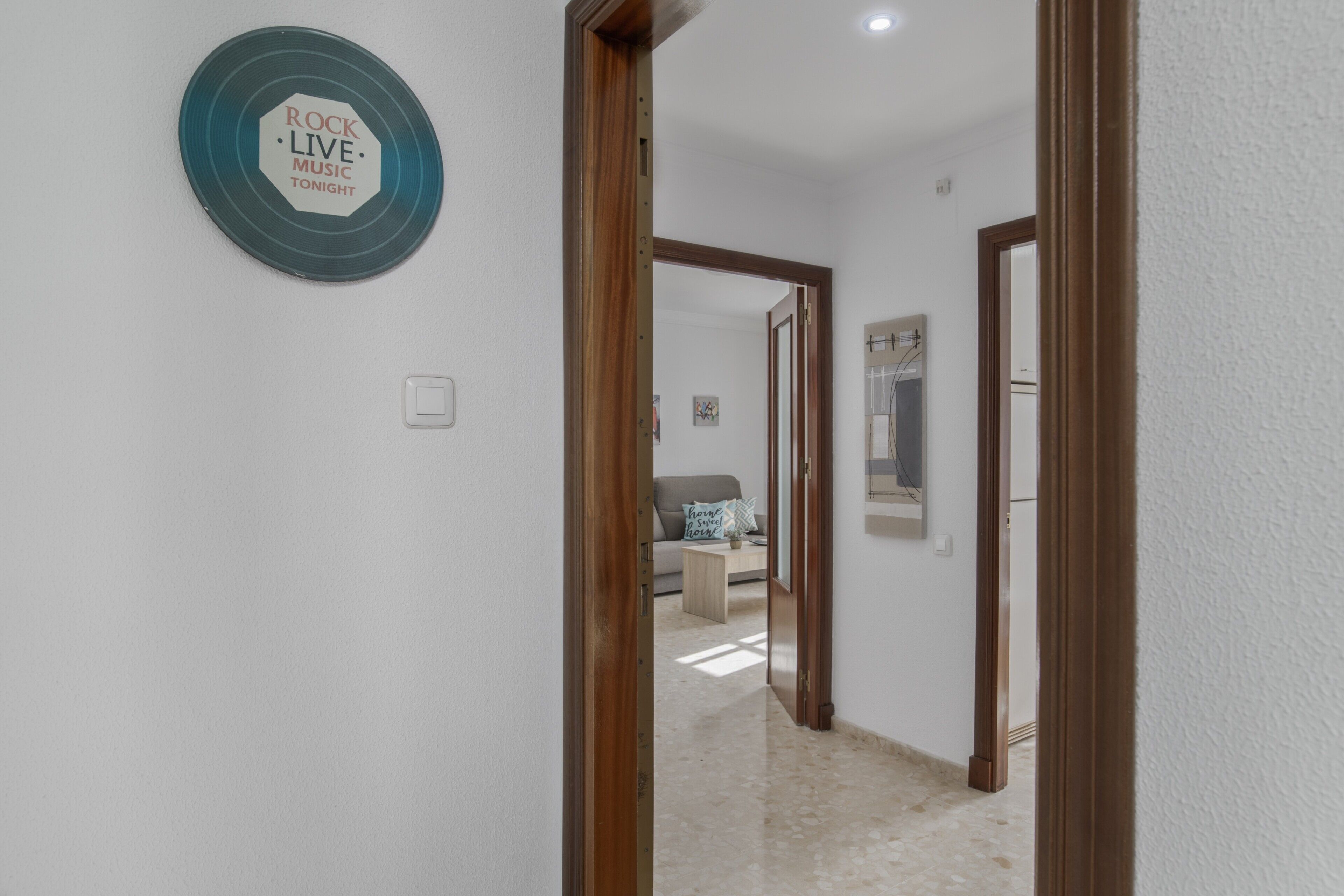 Un couloir avec une porte donnant sur un espace de vie, un panneau fixé au mur et un interrupteur.