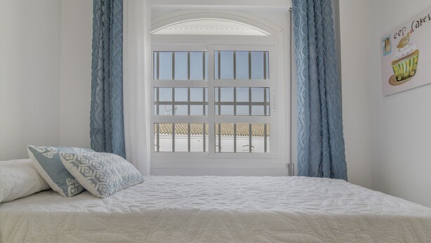 Une chambre à coucher avec un lit, une fenêtre avec des rideaux et un mur orné d’un tableau.