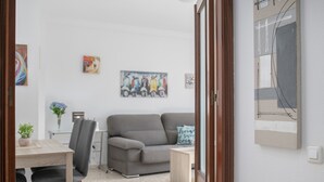 Un salon moderne avec un canapé gris, une petite table et un fauteuil. Des tableaux ornent le mur et une plante en pot est posée sur le sol.