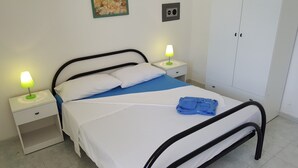 Un llit ben fet amb roba de llit blanca i blava, dues làmpades de nit, una tovallola blava doblegada i un armari blanc.