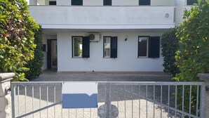 Edifici de dues plantes amb façana blanca, persianes negres i entrada tancada per una reixa.