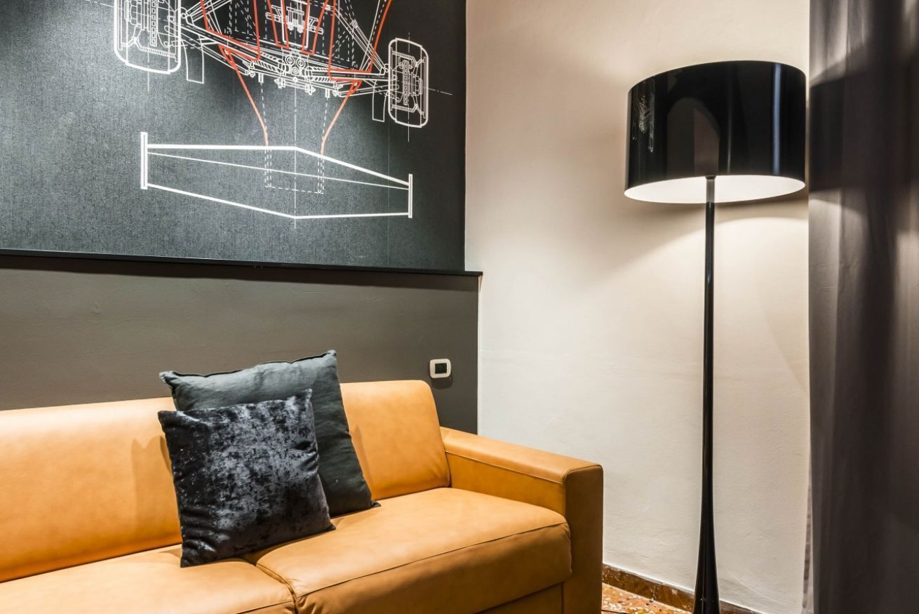 Een moderne woonkamer met een leren bank, een zwarte vloerlamp en een groot abstract kunstwerk aan de muur.