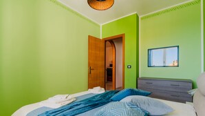 A bedroom with a bed, a nightstand, a dresser, a mirror, and a door leading to another room. - Seaside Holiday in Otranto - Virginia Deluxe (Otranto)