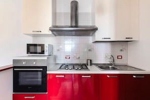 Une cuisine équipée d’un four à micro-ondes, d’un four traditionnel, d’une cuisinière à gaz, d’un évier en acier inoxydable et de meubles de rangement rouges.