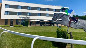 Un bâtiment moderne, avec une enseigne indiquant « L’Hippodrome », et une statue de cheval en premier plan.