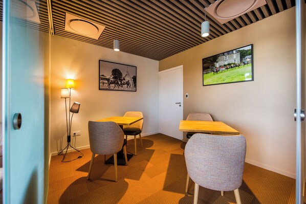 A conference room with two tables, four chairs, a standing lamp, and two wall-mounted light fixtures.