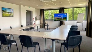 Une salle de conférence avec une longue table, des chaises noires, un écran affichant le mot « Bienvenue » et une vue sur la verdure grâce à de grandes fenêtres.