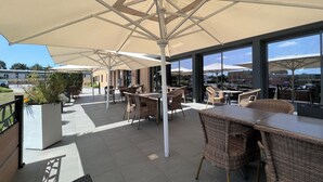 Un espace extérieur aménagé en terrasse, avec des meubles en osier et de grands parasols pour créer de l’ombre.