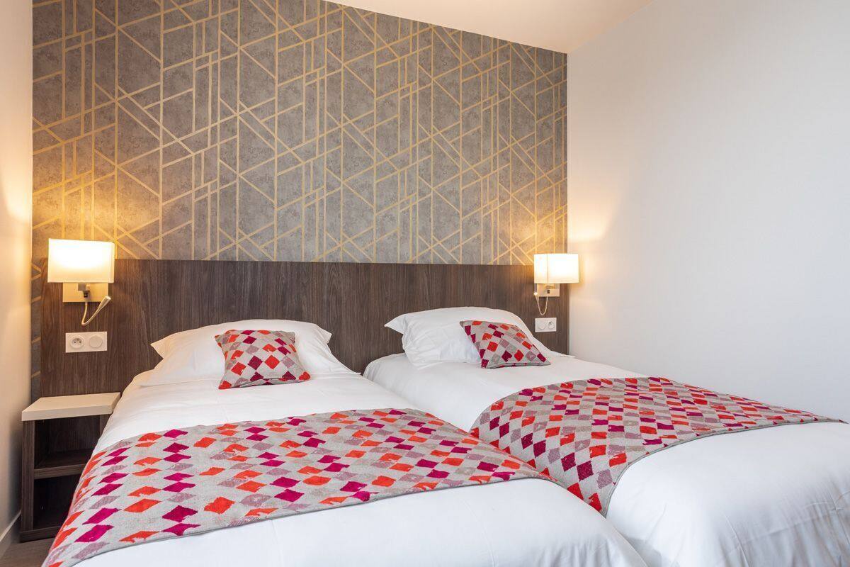 Een hotelkamer met twee bedden, een behang met patroon en bedlampjes.