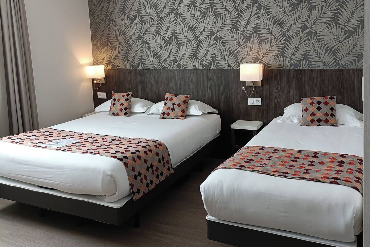 Een hotelkamer met twee bedden, elk voorzien van een beddegoed met een patroon, een hoofdbord met een bladmotief en nachtlampjes.