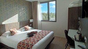 Une chambre d’hôtel équipée d’un lit, d’un bureau, d’une chaise, d’une télévision et d’une fenêtre donnant sur un paysage verdoyant.
