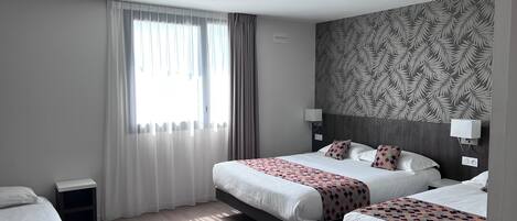 A hotel room with two beds, a large window with sheer curtains, a patterned wallpaper, and a ceiling-mounted security camera.