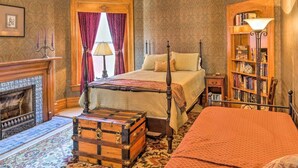 A traditional bedroom with a four-poster bed, a wooden chest, a fireplace, and a bookshelf.