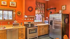 A kitchen with wooden cabinets, a stainless steel refrigerator, a stove, and a window with a curtain.