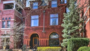 A red brick building with two-story windows, a front entrance with a door, and a small set of steps leading up to the entrance.